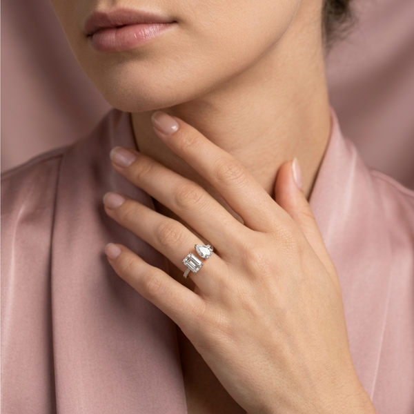 18K solid gold emerald and pear cut diamond toi et moi engagement ring styled on hand with pink silk
