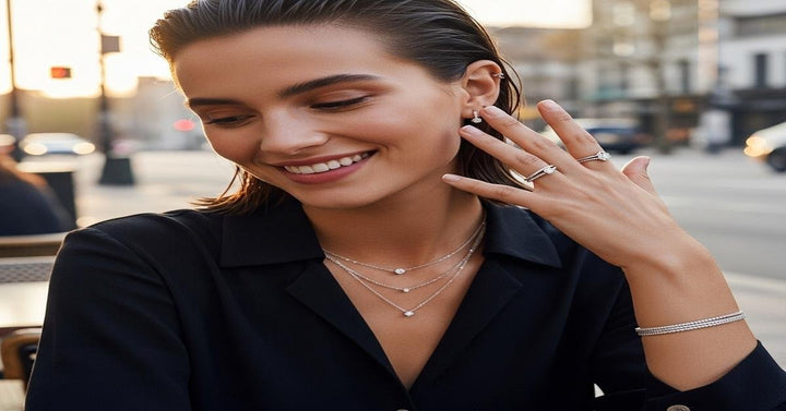 Young woman wearing layered diamond necklaces, stacked rings, and tennis bracelet in a modern setting - Riyanika Jewels